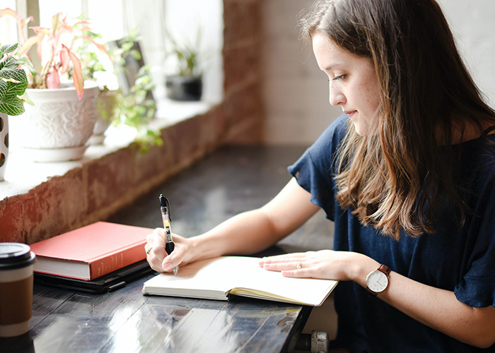 Training-Programme-Knowledge Young woman sat at a desk and writing in a notebook